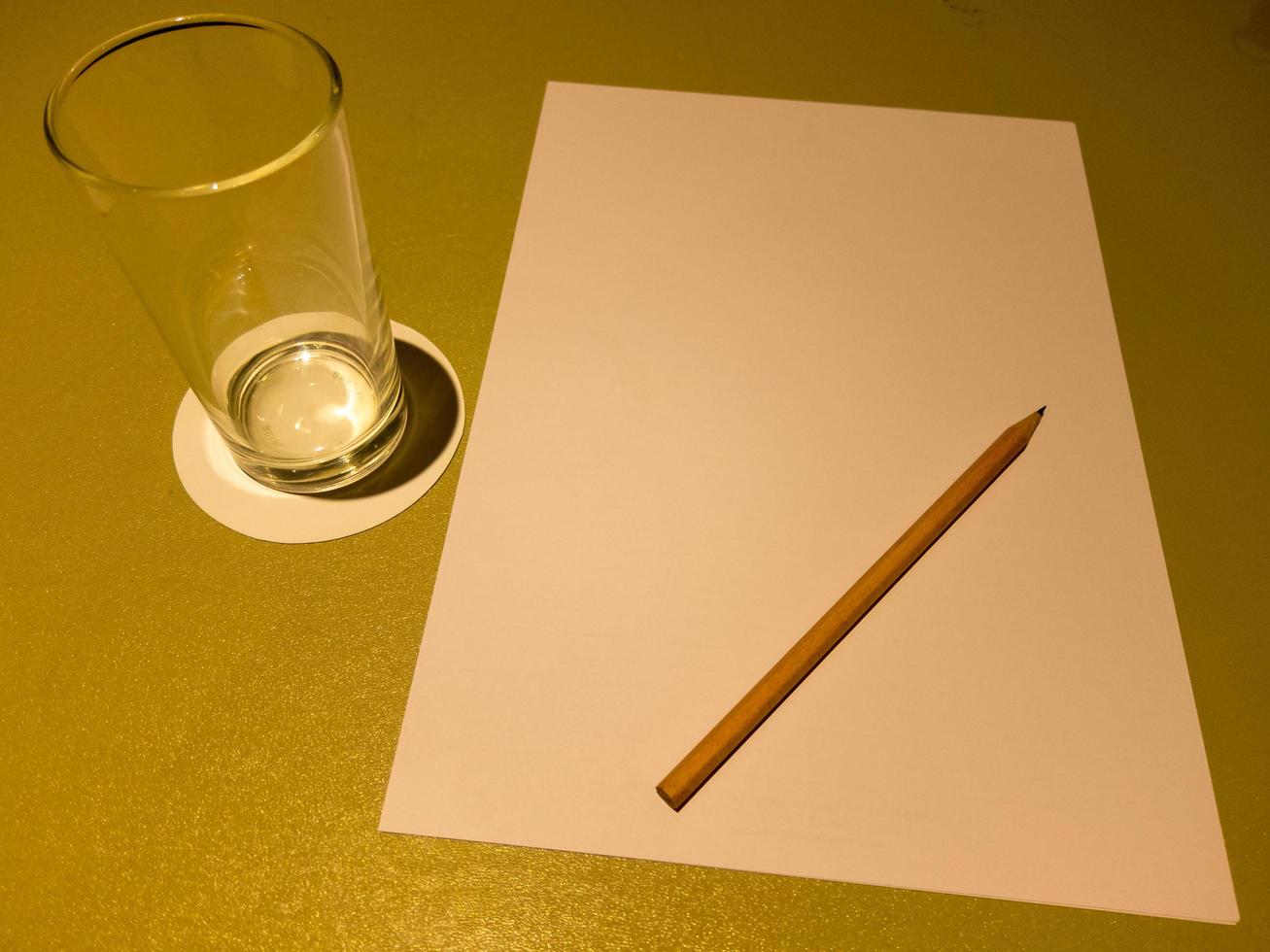 op tafel staan een glas a4 papier water en bruine houten potloden. foto
