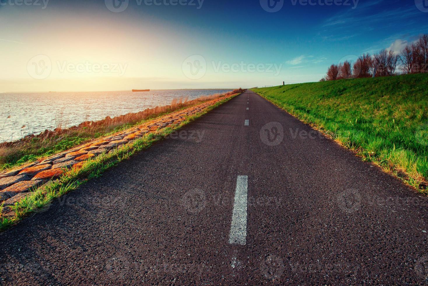 asfaltweg langs de zee bij zonsondergang foto