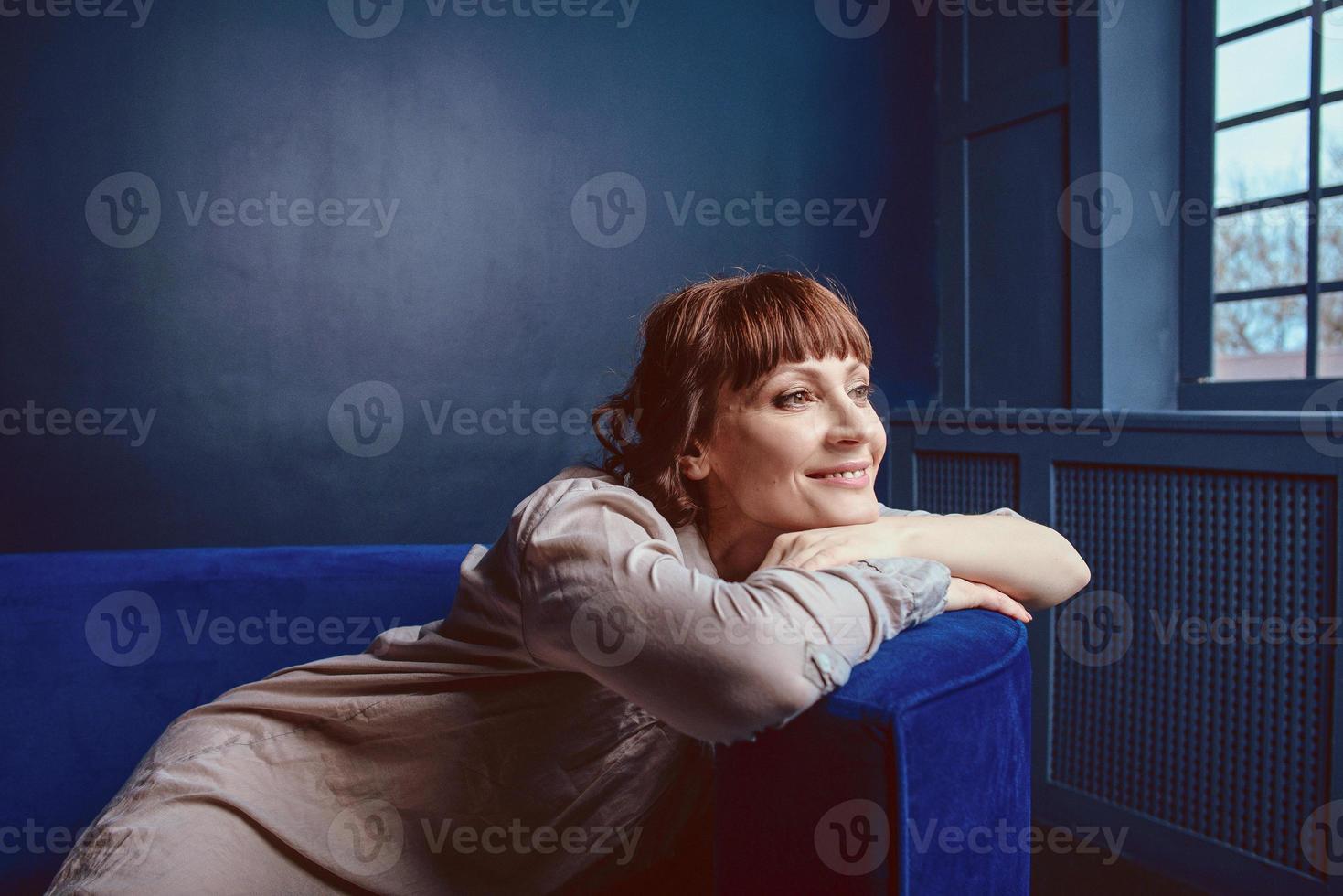 mooie ontspannen vrouw thuis interieur in de buurt van de blauwe sofa foto