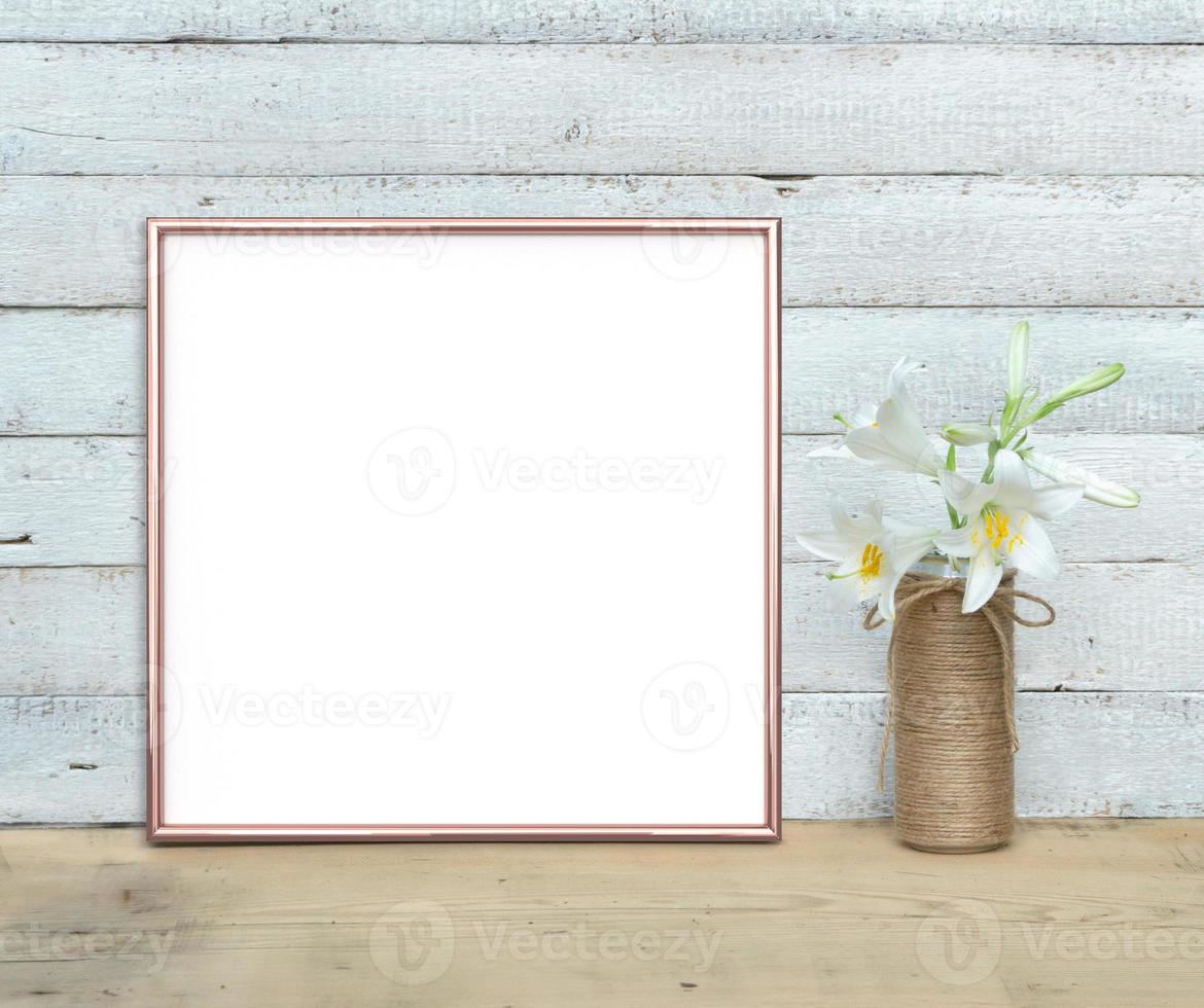 rose gouden vierkante frame mockup in de buurt van een boeket lelies staat op een houten tafel op een geschilderde witte houten achtergrond. rustieke stijl, eenvoudige schoonheid. 3 renderen. foto