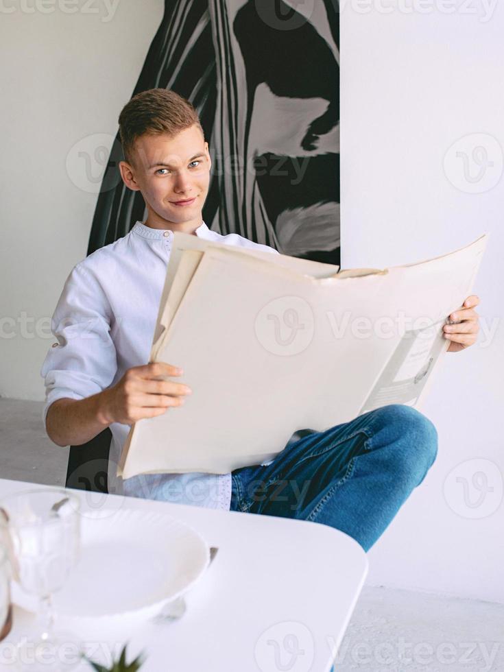 moderne tiener man leest papieren krant tijdens het ontbijt thuis. lezen, ouderwets, modern, nieuwsconcept foto