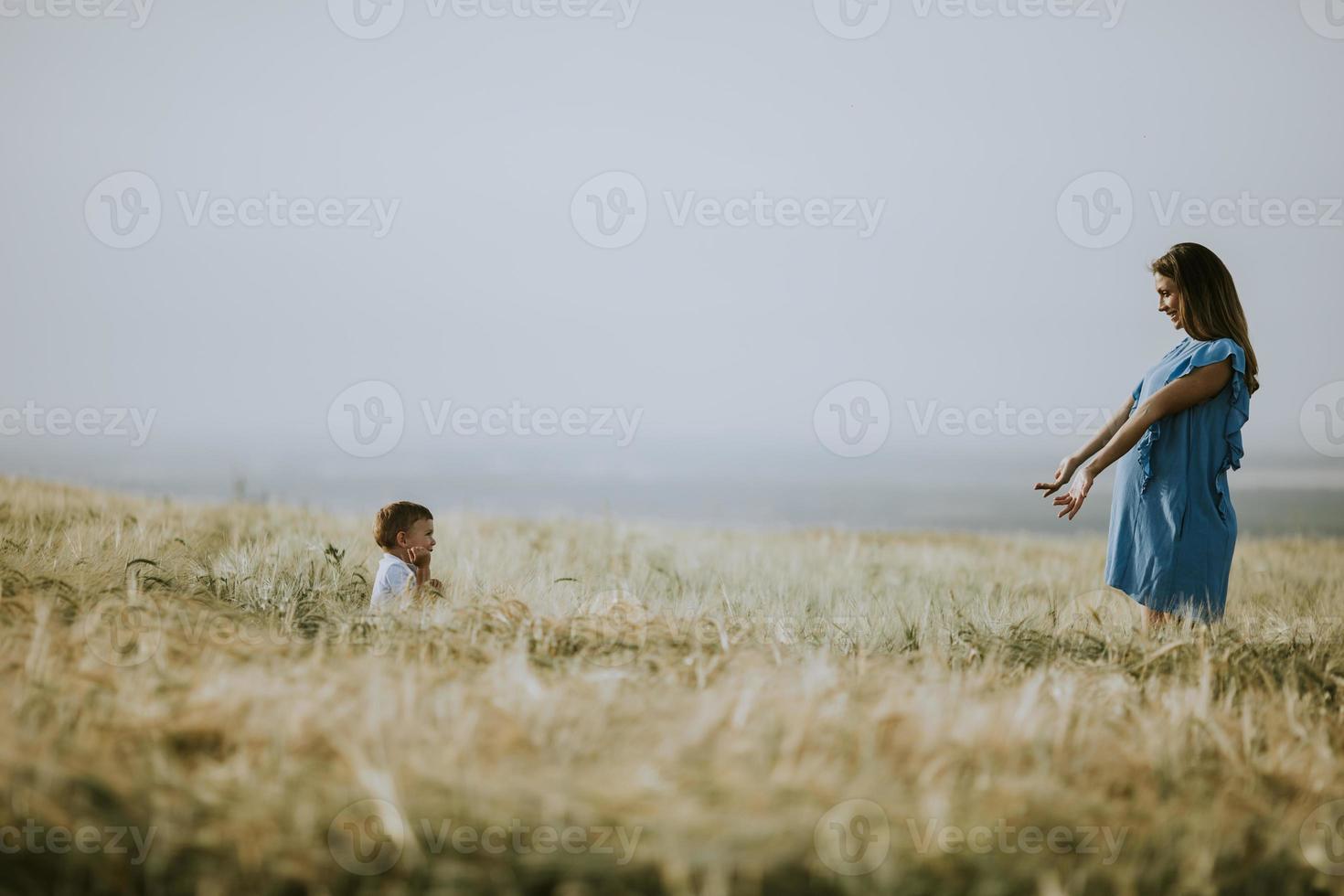 jonge zwangere moeder met haar schattige kleine jongen in het veld op een mooie zonnige dag foto