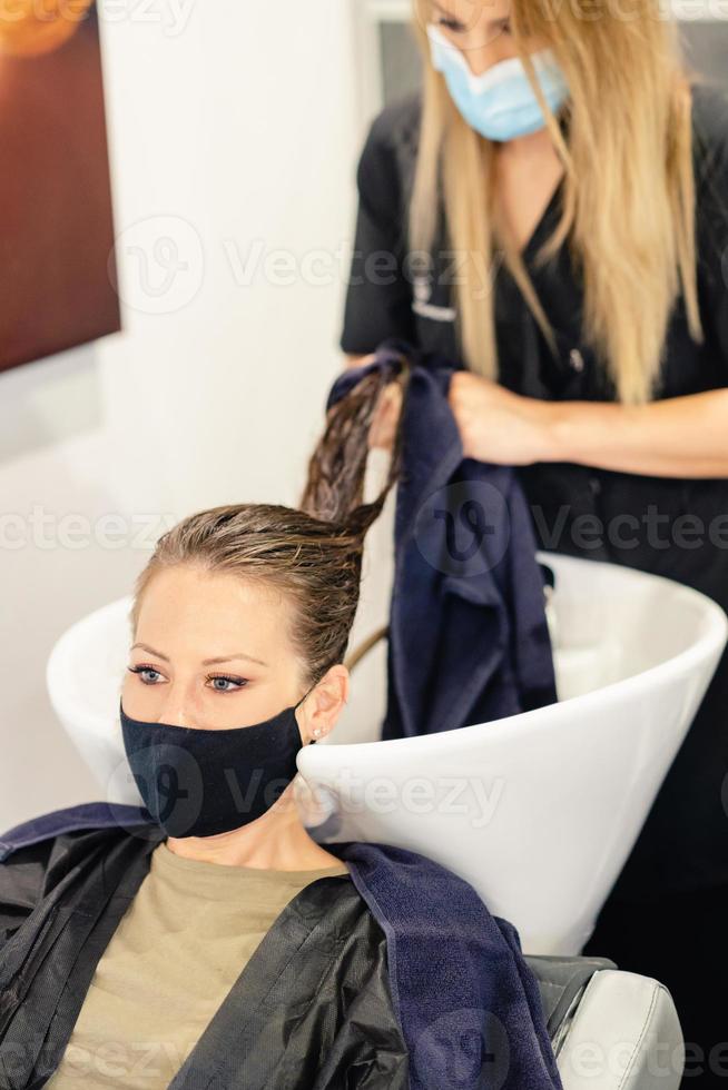 vrouwelijke kapper die het hoofd van een klant wast in een salon, beschermd door een masker foto