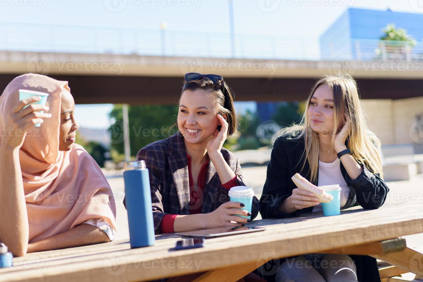 glimlachende diverse jonge vrouwen die koffiepauze hebben en kletsen in het stadspark foto