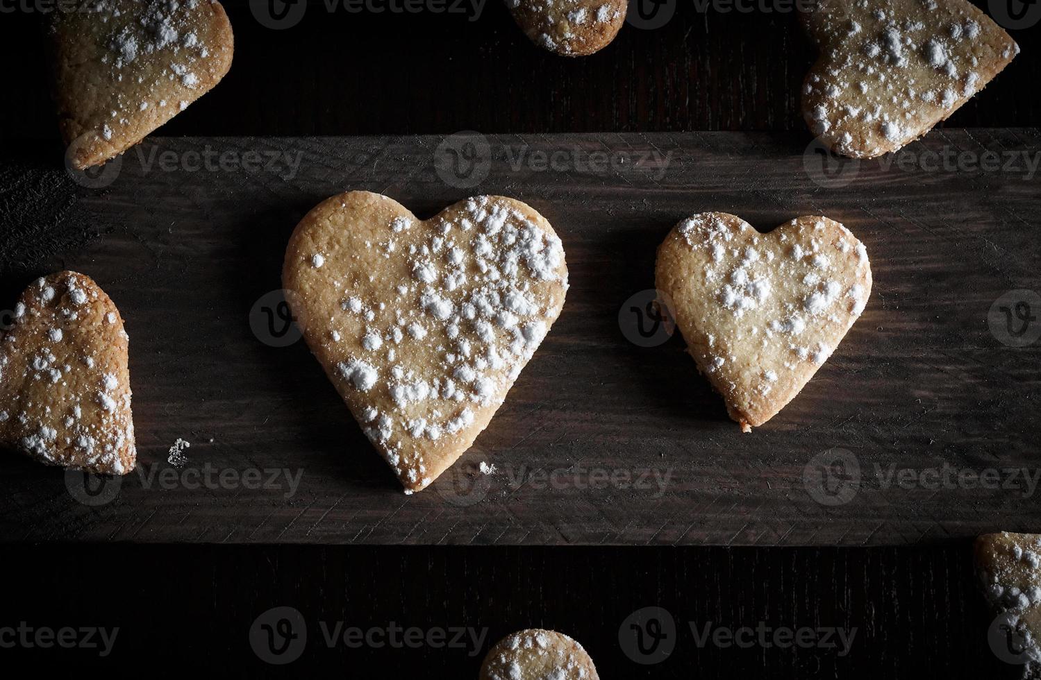 heerlijke zelfgemaakte hartvormige koekjes bestrooid met poedersuiker in een houten plank. horizontaal beeld van bovenaf gezien. donkere humeurige stijl. foto