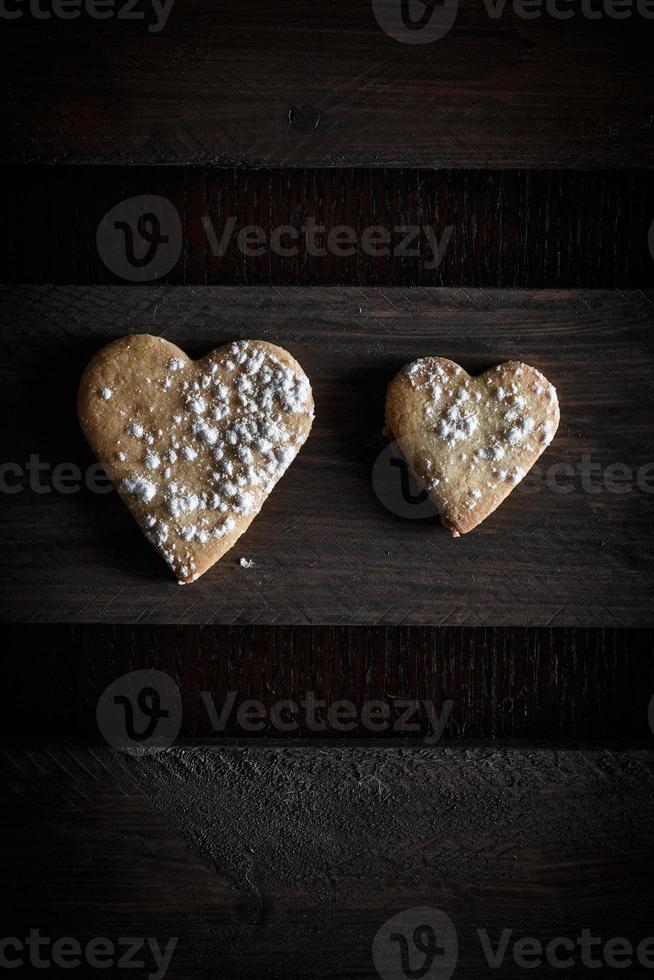 twee heerlijke zelfgemaakte hartvormige koekjes bestrooid met poedersuiker in een houten plank. verticaal beeld van above.concept van liefde in paar. donkere humeurige stijl. foto