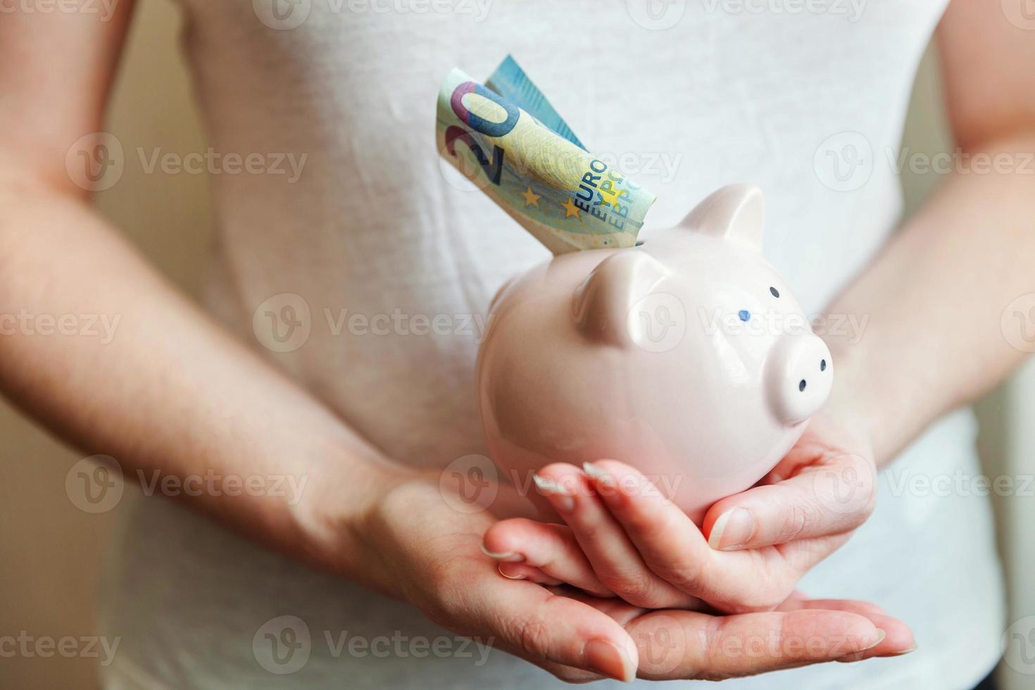 vrouwelijke vrouwenhanden die roze spaarvarken houden en geldeuro zetten. besparing investeringsbudget zakelijke rijkdom pensioen financieel geld bankconcept. foto