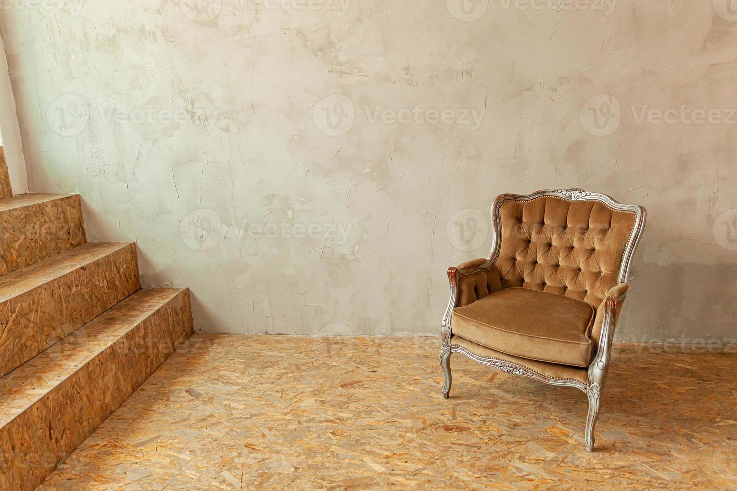 mooie luxe klassieke biege schone binnenkamer in grunge-stijl met bruine barokke fauteuil. vintage antieke bruin-grijze stoel die naast de muur staat. minimalistisch huisontwerp. foto