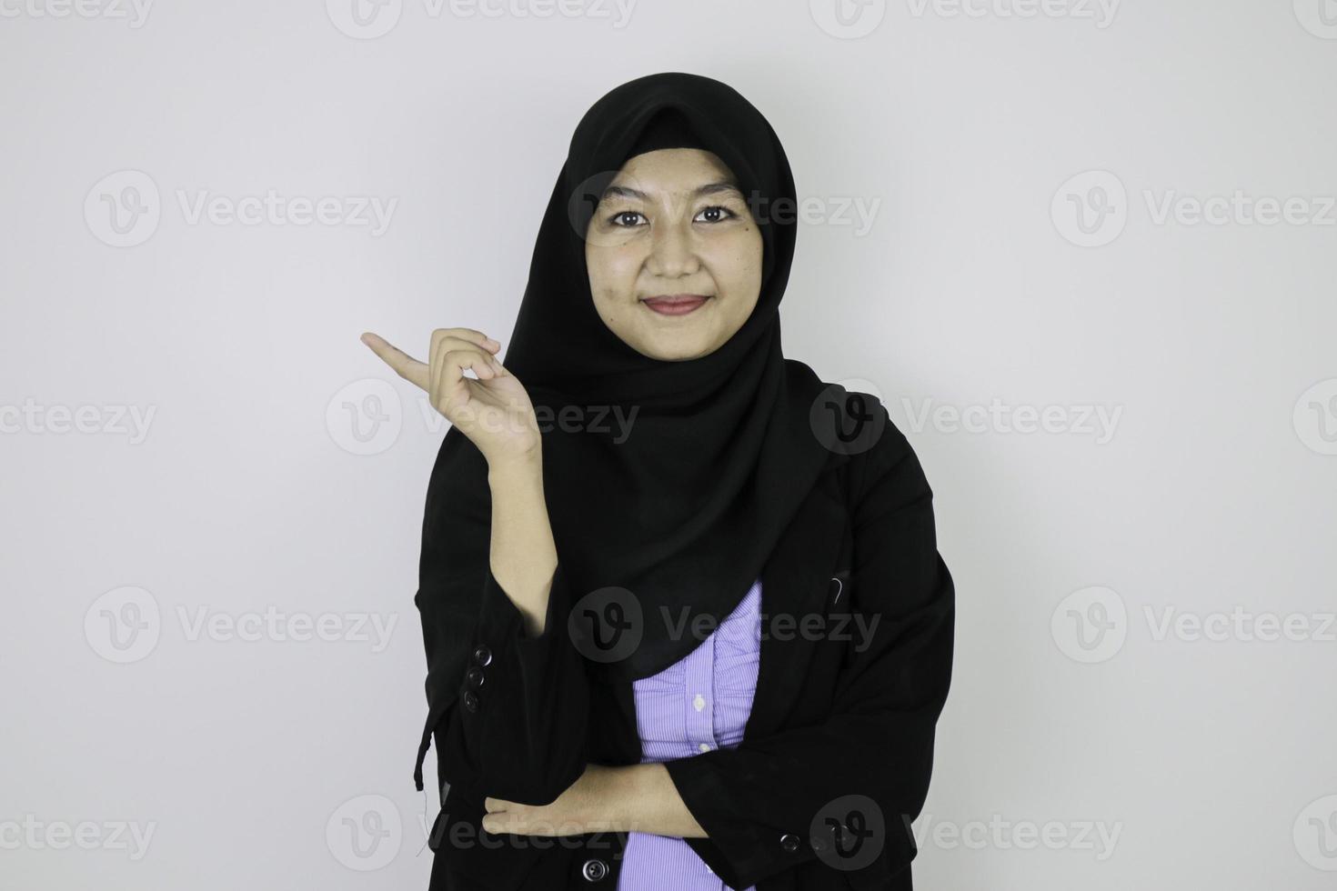 gelukkige jonge aziatische islamvrouw die een hoofddoek draagt, glimlacht en wijst ernaast. foto