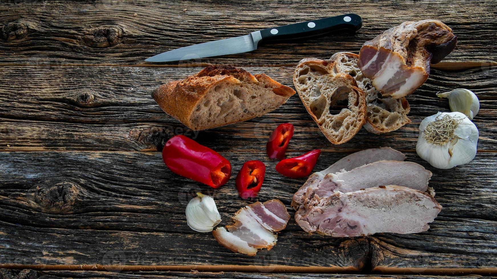 oude rustieke houten tafel met brood, vlees, spek, rode peper en knoflook van bovenaf foto