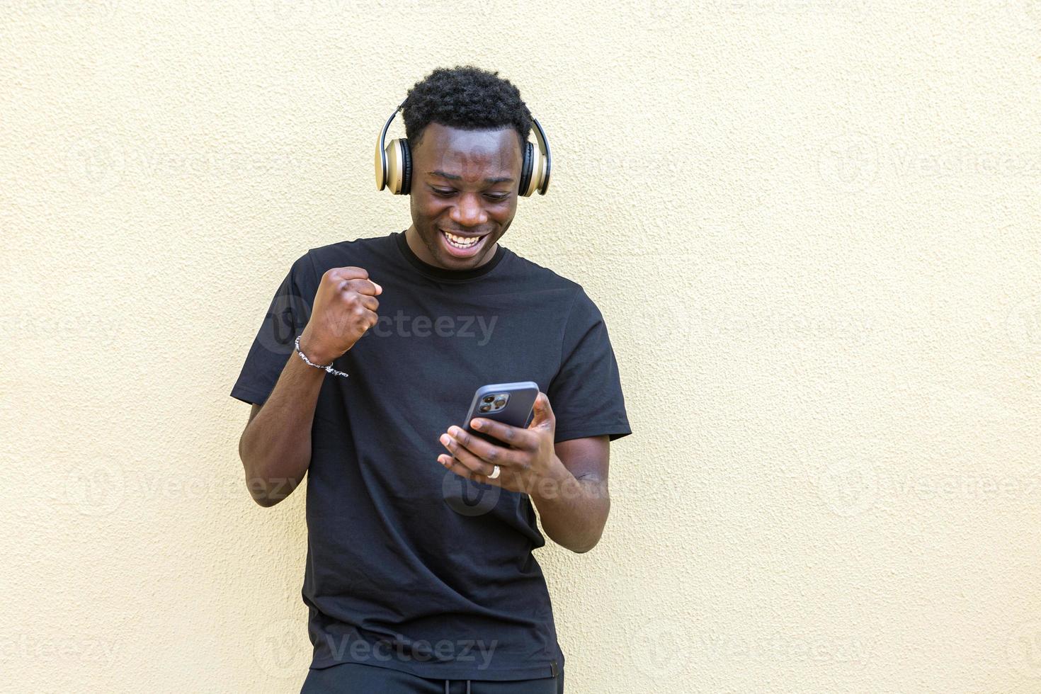 vrolijke jonge zwarte man balde vuist en glimlachen tijdens het gebruik van smartphone op straat foto