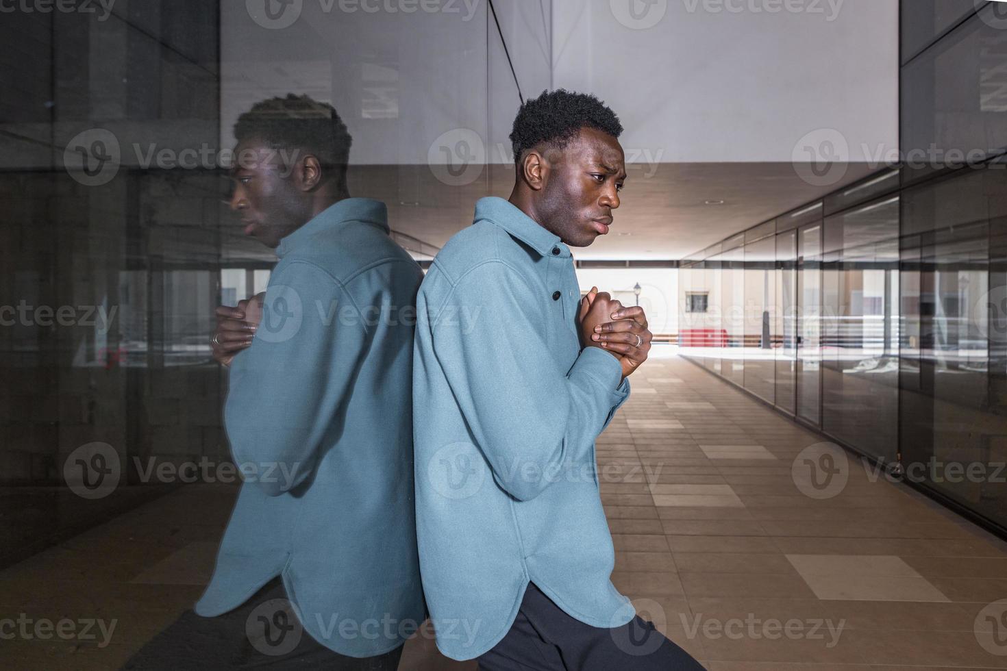 ongelukkige jonge zwarte man die in de doorgang bij de glazen wand staat foto
