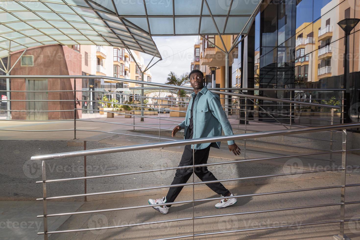 coole Afro-Amerikaanse man die in de buurt van een modern gebouw loopt en wegkijkt foto