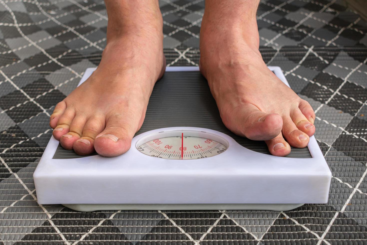 een jonge man wordt blootsvoets op de weegschaal gewogen om zijn gewicht onder controle te houden en een dieet te volgen foto