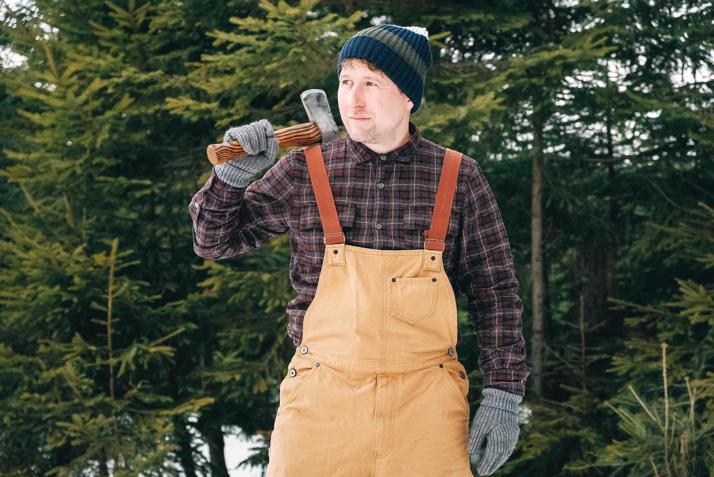 portret van een man houthakker met een bijl in zijn handen op een achtergrond van bos en bomen foto