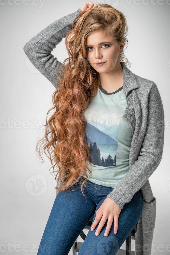 modieuze vrouw die zich voordeed op een witte achtergrond, stijlvolle kleding jeans en t-shirt met gebreid jasje foto