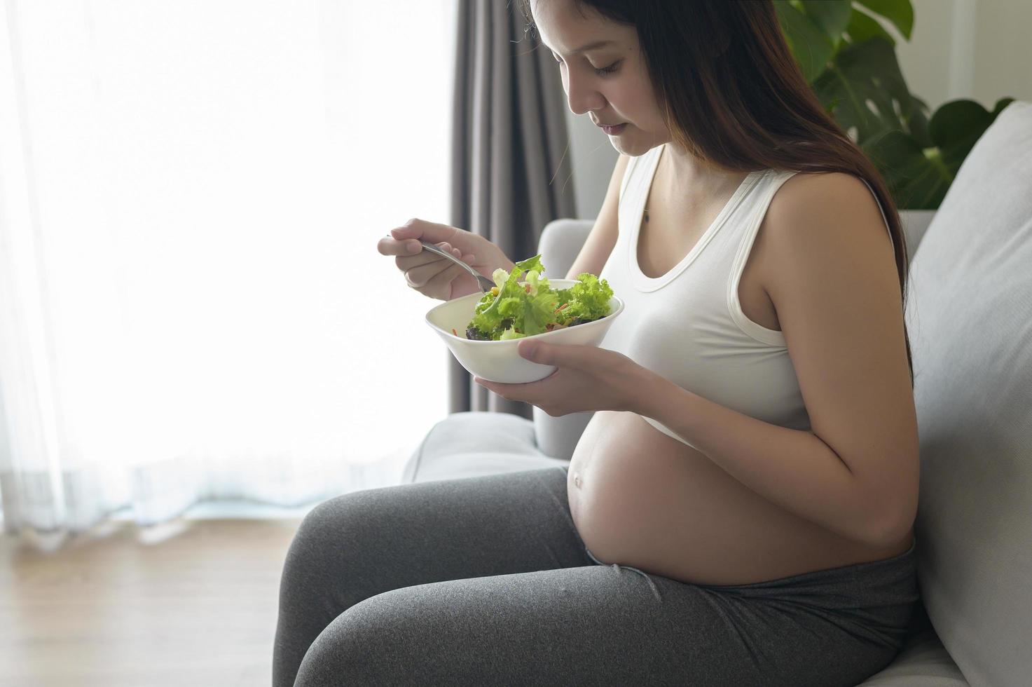 jonge zwangere vrouw met salade thuis, gezondheidszorg en zwangerschapszorg foto