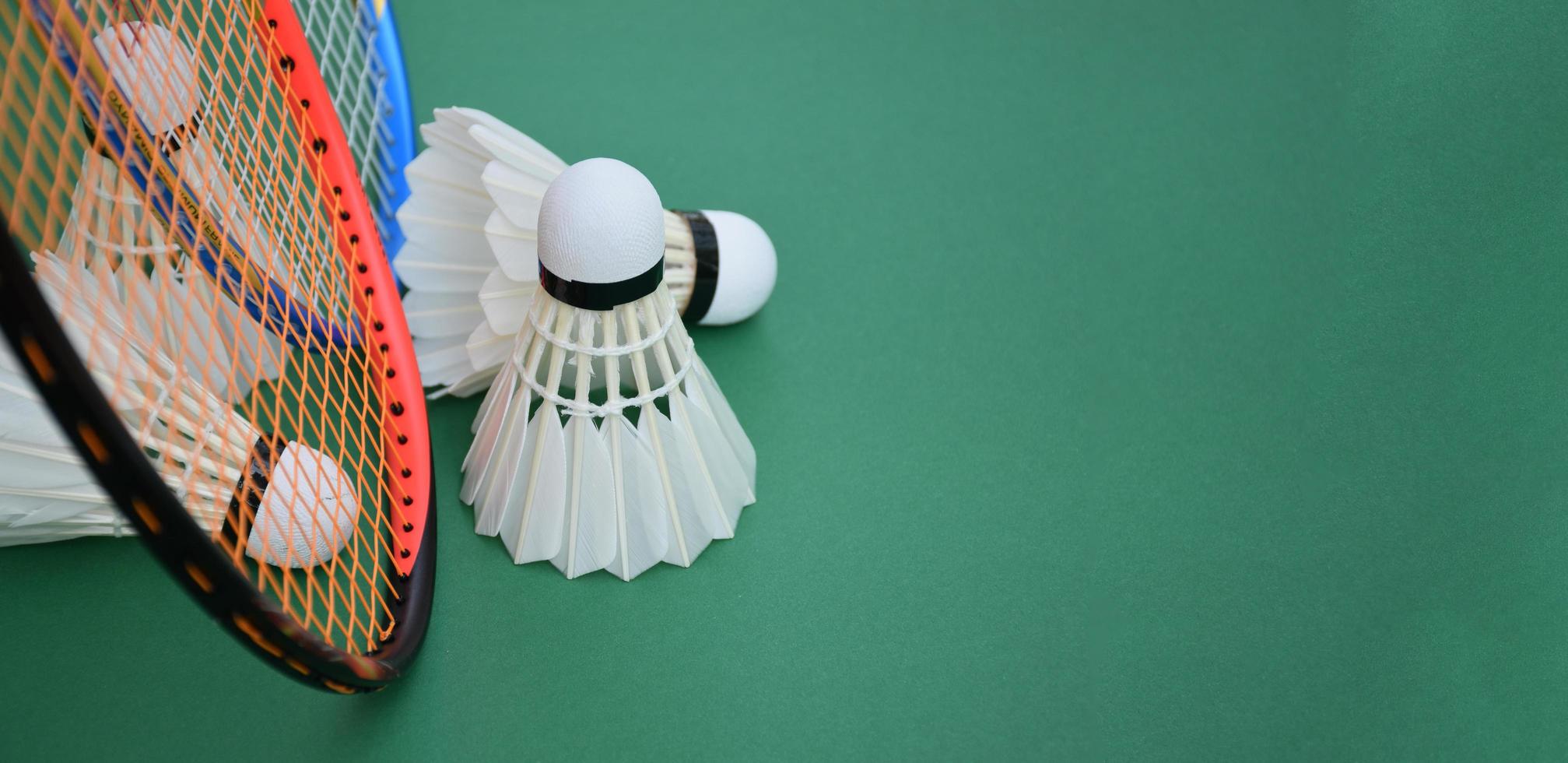 roomwitte badmintonshuttle en racket met neonlichtschaduw op groene vloer in indoor badmintonveld, vage badmintonachtergrond, kopieerruimte. foto