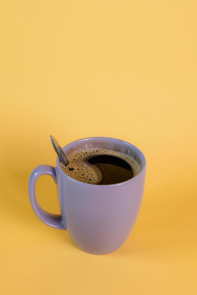 paarse mok met hete zwarte koffie met een paar bubbels op een gele achtergrond, genomen in een studio. foto