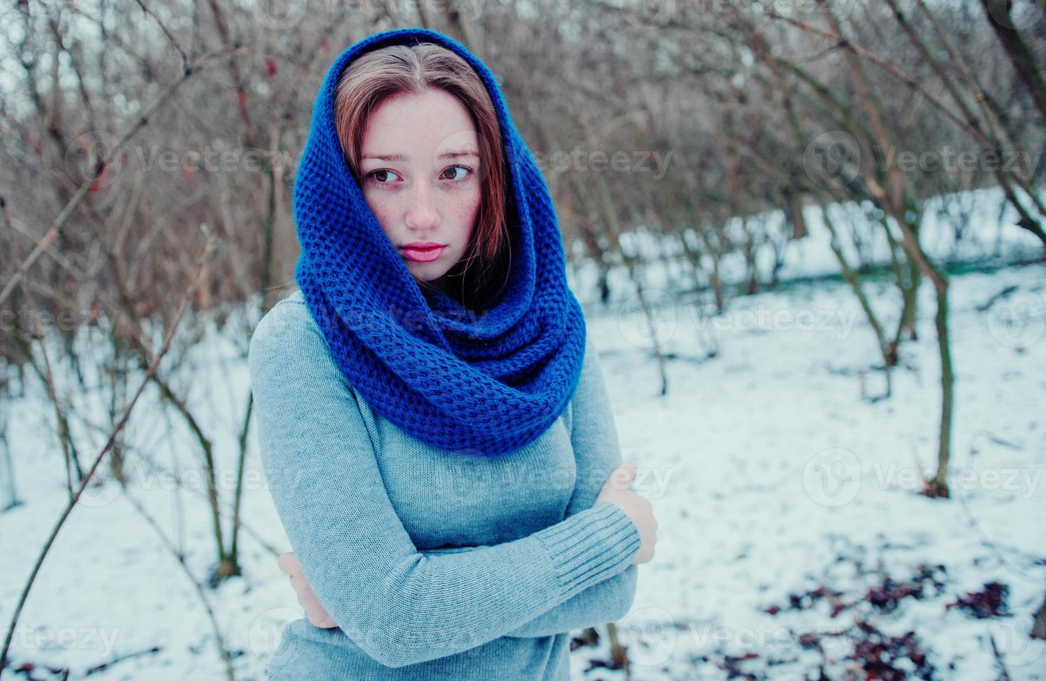 portret van een jong rood haarmeisje met sproeten die een blauwe gebreide wollen sjaal dragen in de winterdag. foto