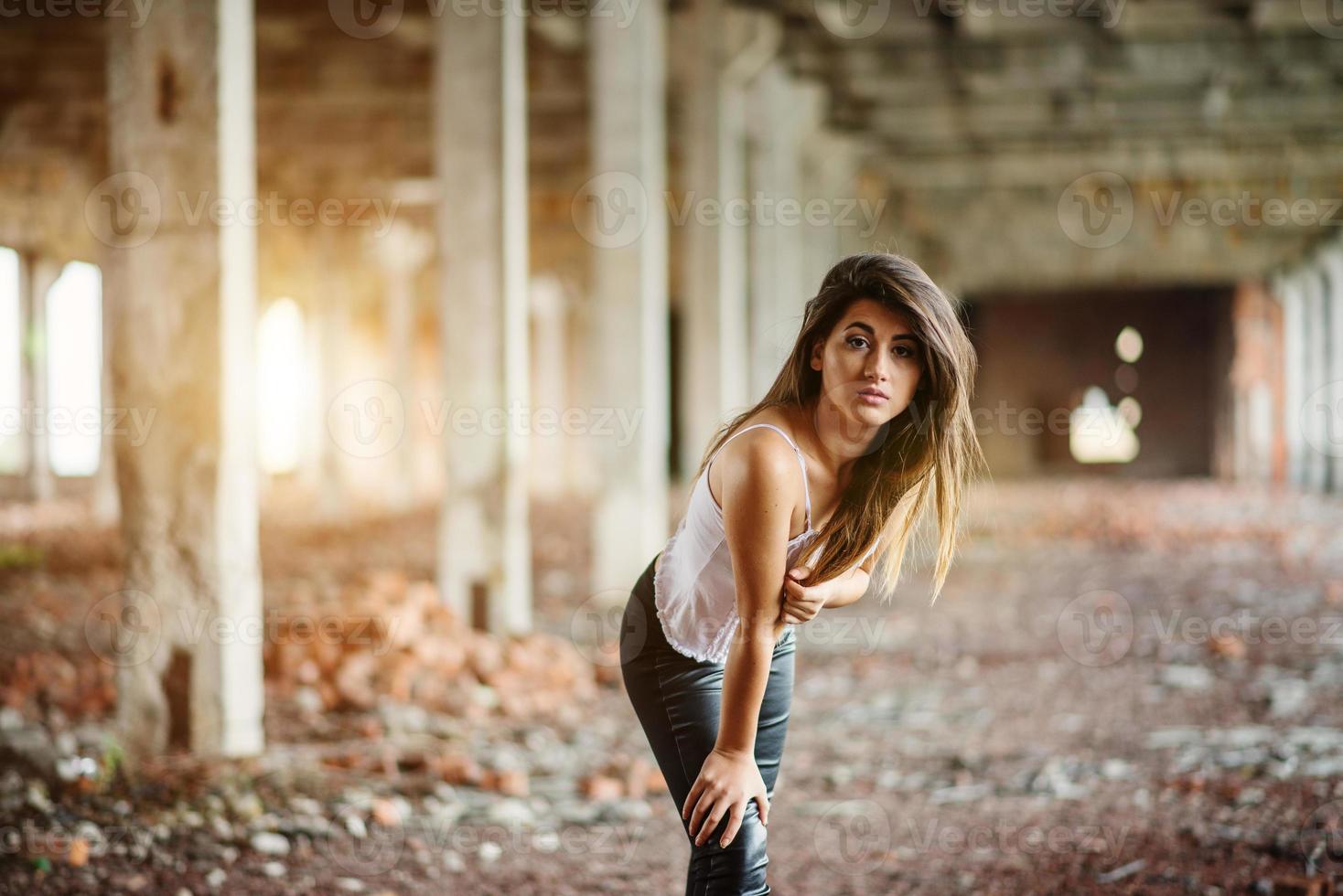 portret van een jong schattig brunette meisje met een zwarte leren broek en een witte blouse op een verlaten plek. foto