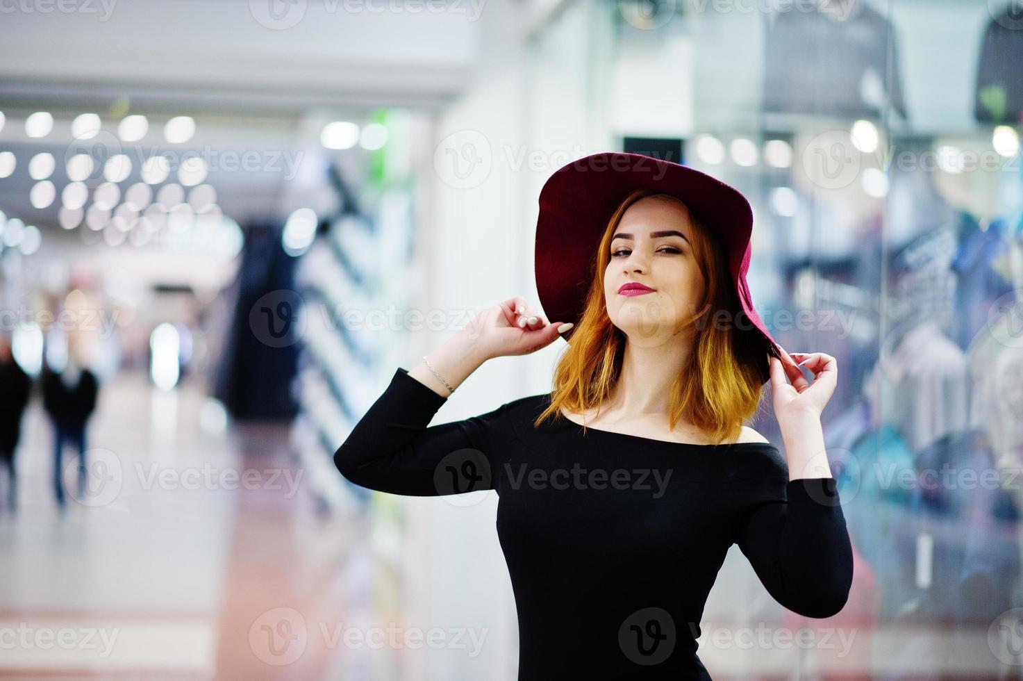mode roodharige meisje slijtage op zwarte jurk en rode hoed gesteld op handel winkelcentrum. foto getinte stijl instagram filters.