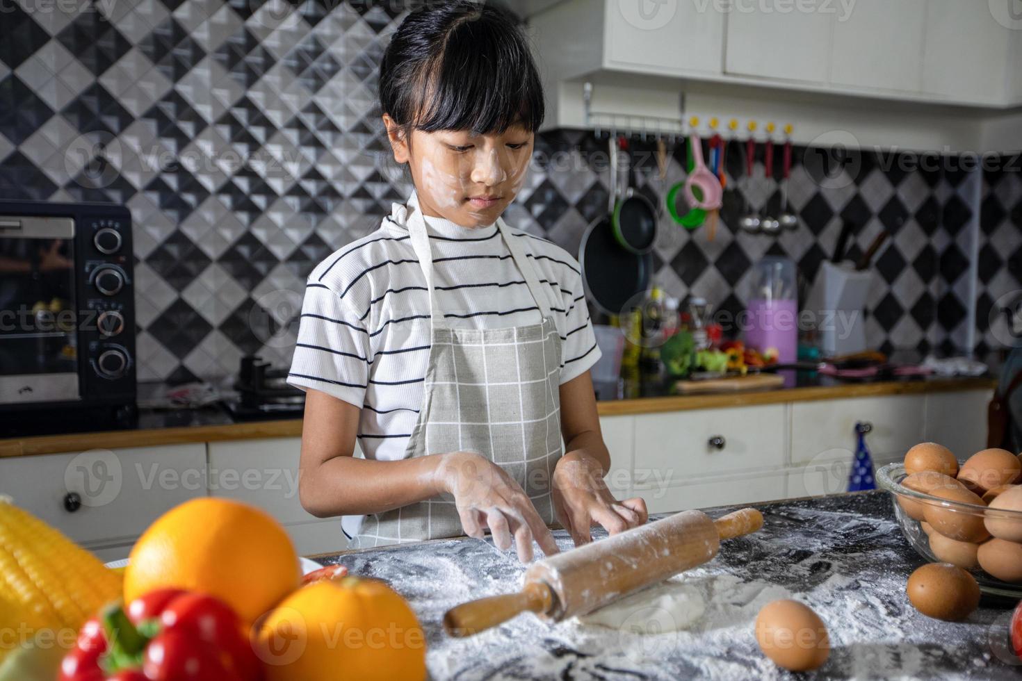 gelukkige familie en hun dochtertje bereiden een pizza, kneed het deeg en legt ingrediënten op de keukentafel foto