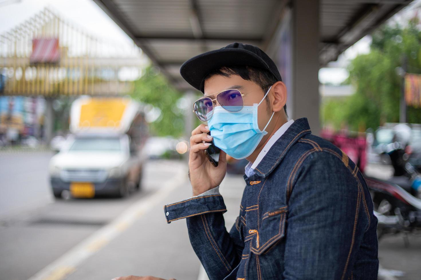 Aziatische jonge man die smartphone in de stad gebruikt en gezichtsmasker draagt voor bescherming tegen luchtvervuiling, deeltjes en voor bescherming griepvirus, griep, coronavirus foto