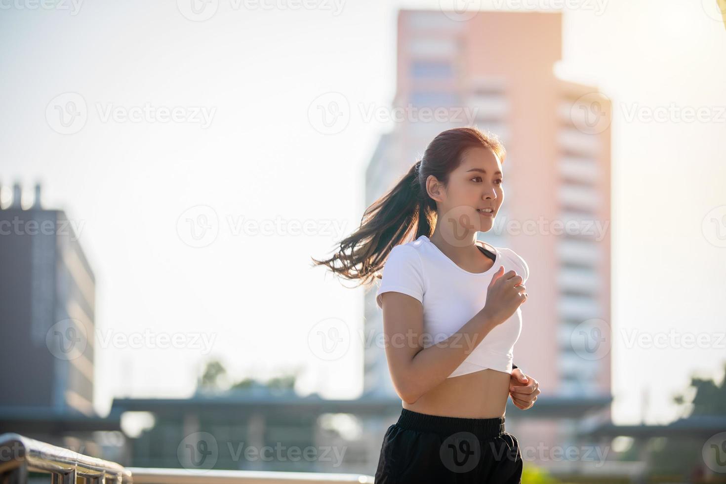 Aziatische jonge fitness sport vrouw rennen en glimlachen op stadsweg foto