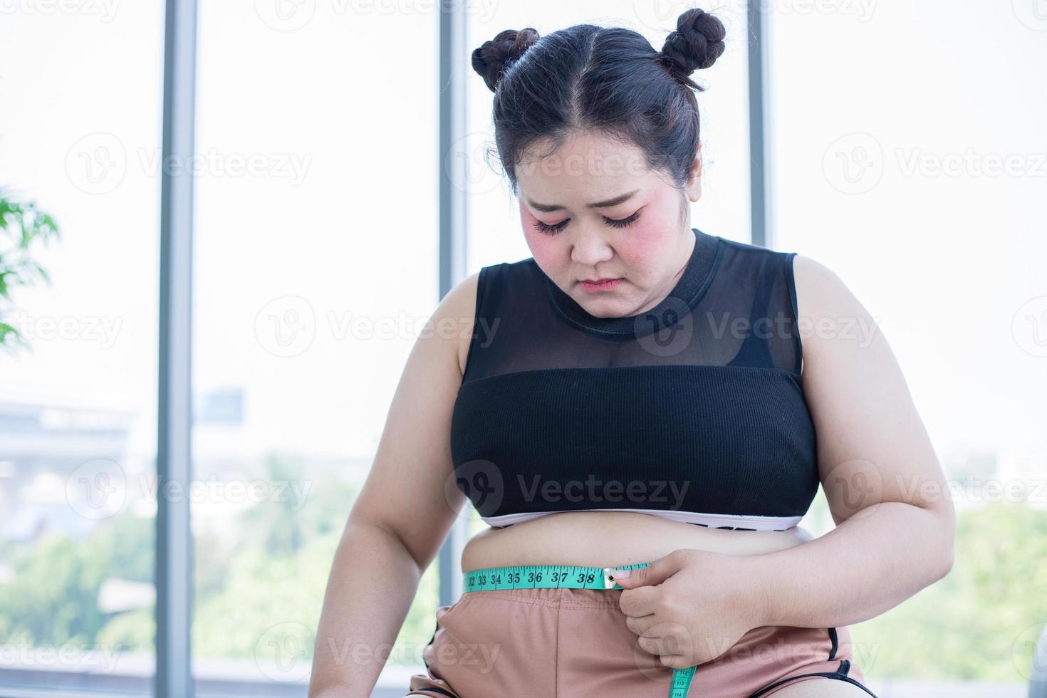Aziatische vrouw met overgewicht die thuis vetlaag met taille meet foto