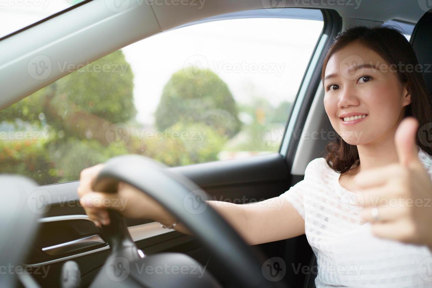 gelukkige aziatische vrouw die het elektrische voertuig bestuurt - ev-auto glimlacht en toont haar duim naar de camera, gelukkig en veilig rijconcept. vrouw moderne ev auto rijden en glimlacht naar de camera. foto