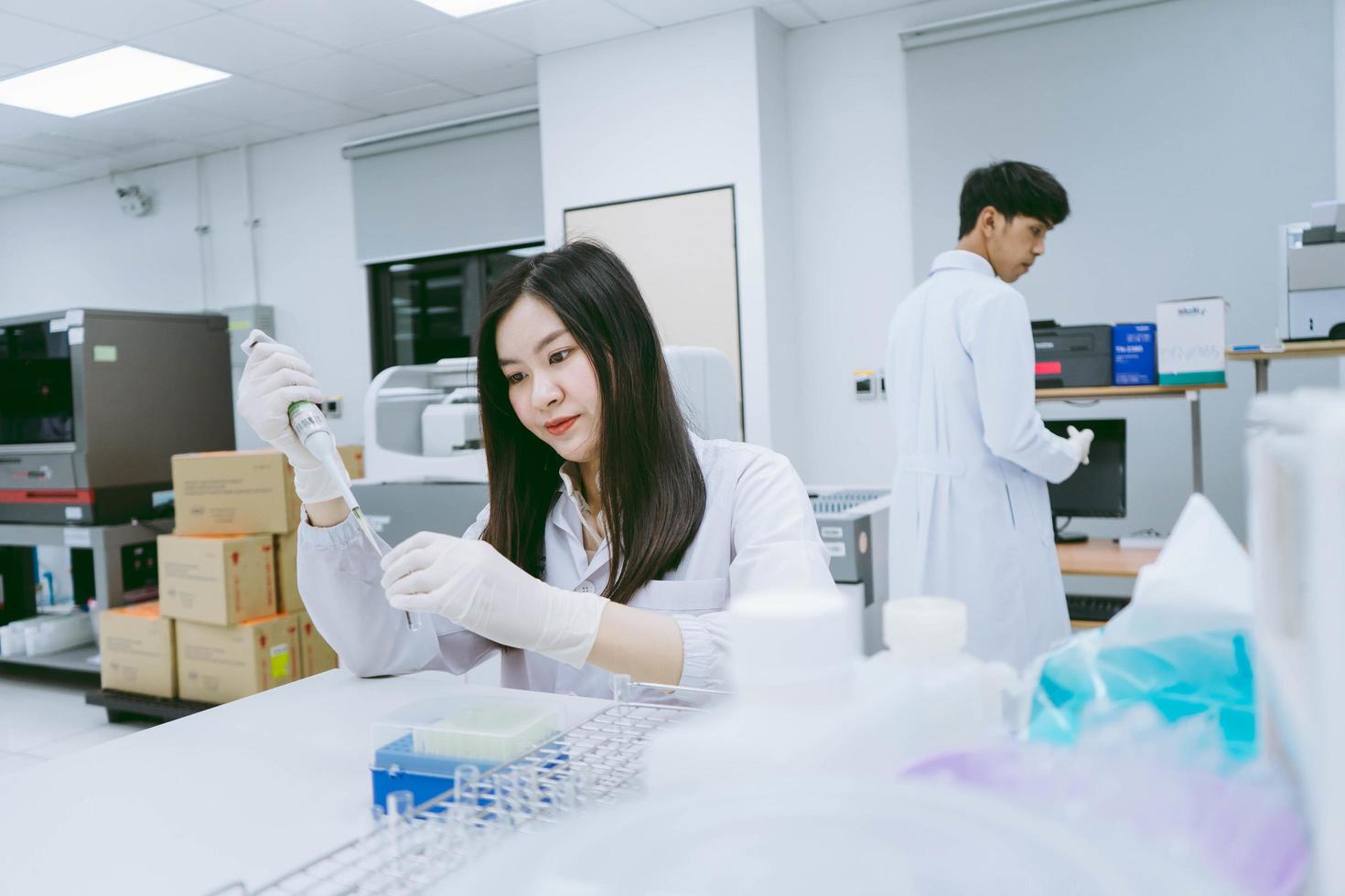 jonge medische wetenschapper die in een medisch laboratorium werkt, jonge vrouwelijke wetenschapper die een automatische pipet gebruikt om het monster over te brengen foto