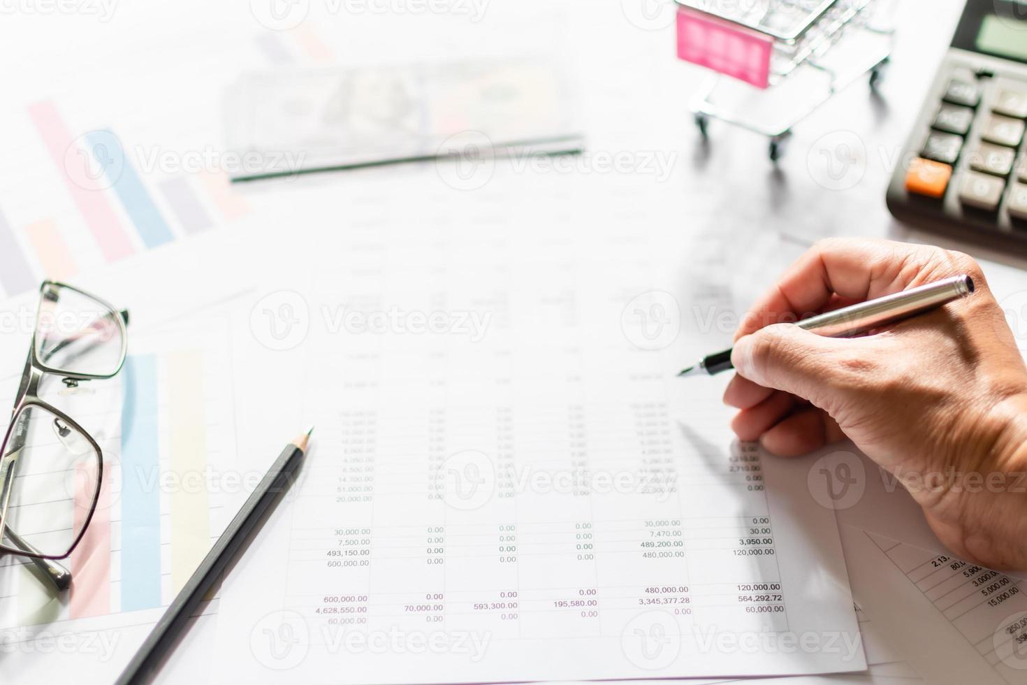 financiële boekhouding, thuiswerken, close-up man's hand met een pen die boekhoudnummers onderzoekt. getallen op papier en rekenmachine, veel getallen, grafiek, potlood, bril op papier, onscherpe achtergrond. foto