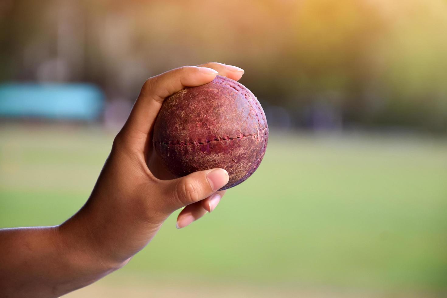 cricketbal voor het oefenen of trainen in de hand, wazig groen grasveld achtergrond, concept voor cricketsportliefhebbers over de hele wereld. foto