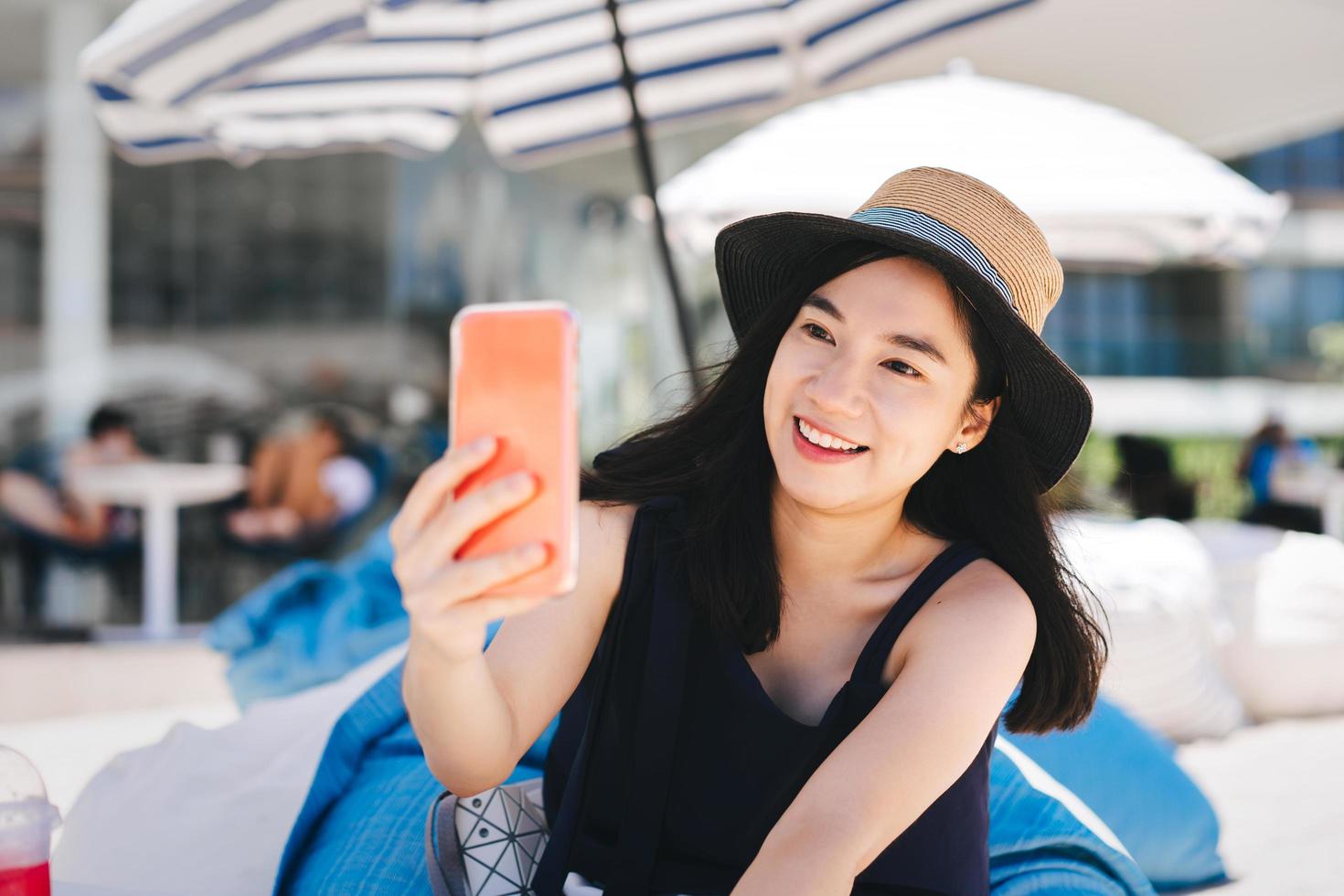 jonge volwassen reiziger Aziatische vrouw selfie per mobiele telefoon in openlucht strandcafé op dag. foto