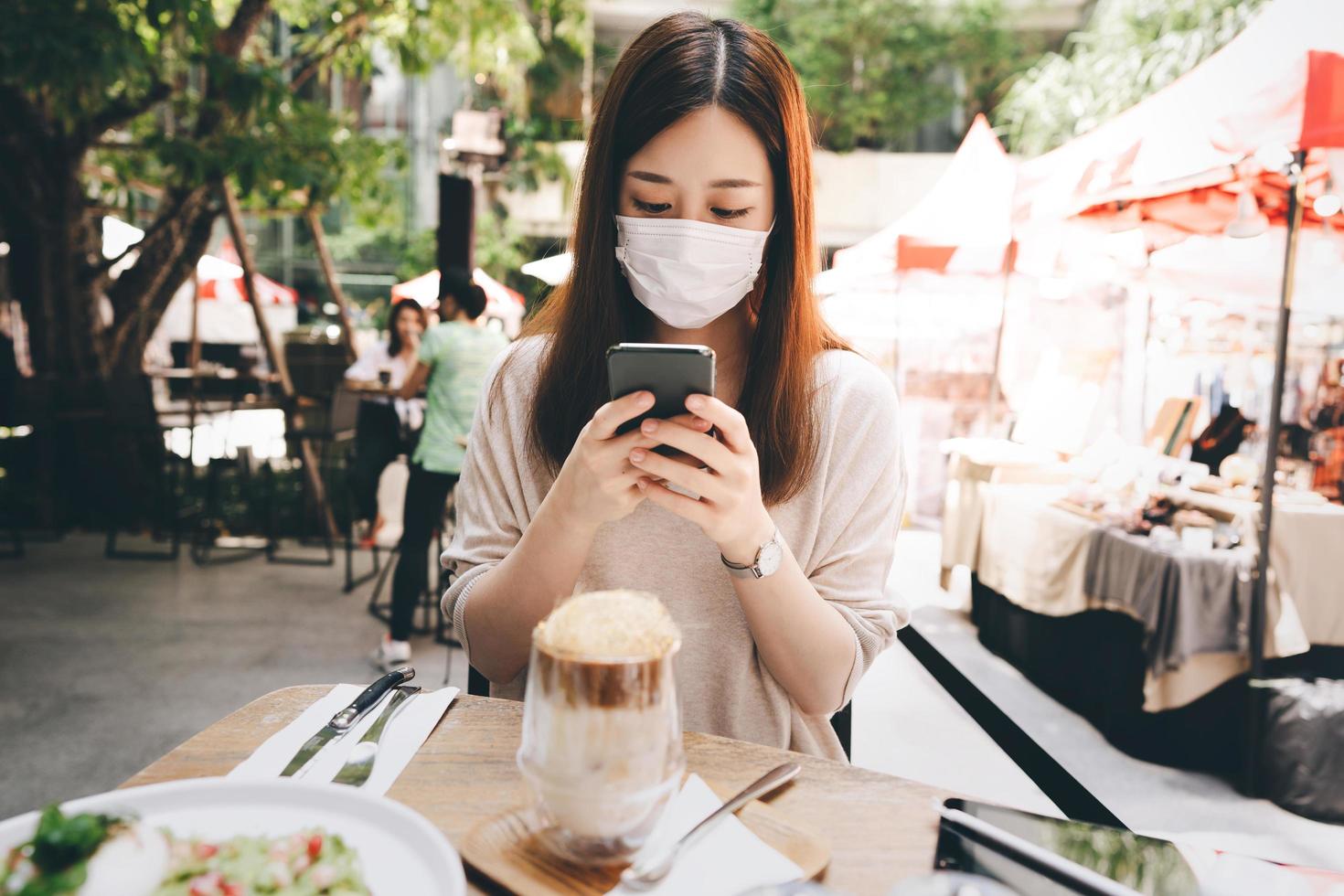 jonge volwassen aziatische vrouw draagt een masker voor een nieuwe normale levensstijl in een openluchtrestaurant op dag foto