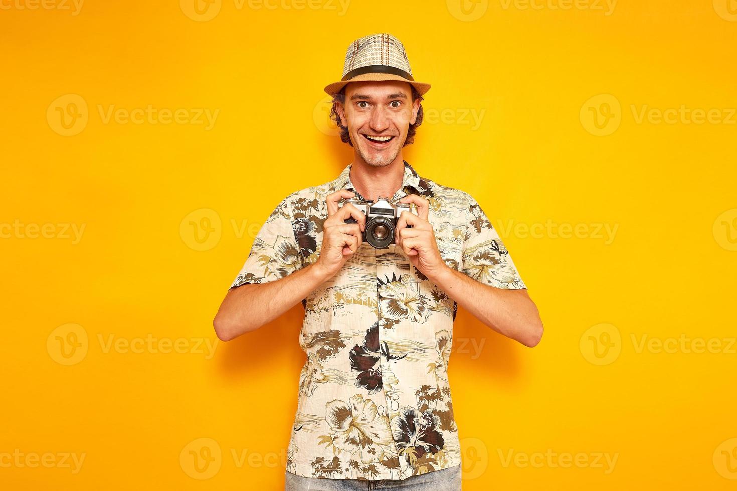 een opgewonden mannelijke toeristische reiziger op vakantie in hoed en hawaiiaans shirt houdt camera voor zich en blij om het resulterende frame te zien. geïsoleerd op gele achtergrond met ruimte voor tekst. concept mensen foto