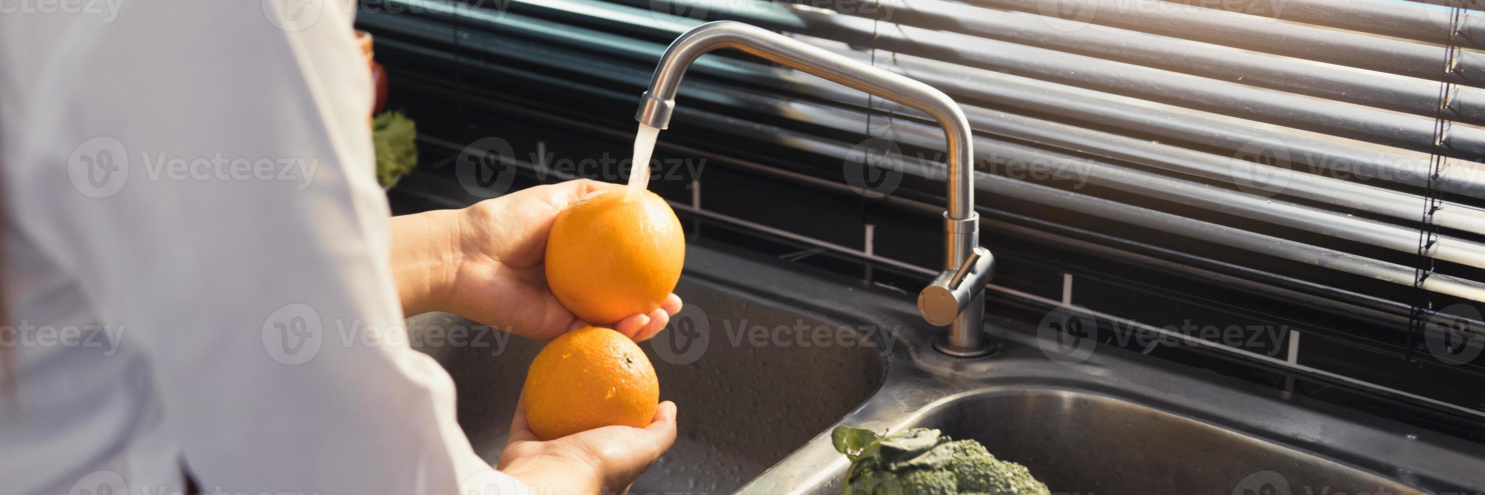 Aziatische handen vrouw wassen fruit sinaasappel en voorbereiding gezond voedsel in de keuken. foto