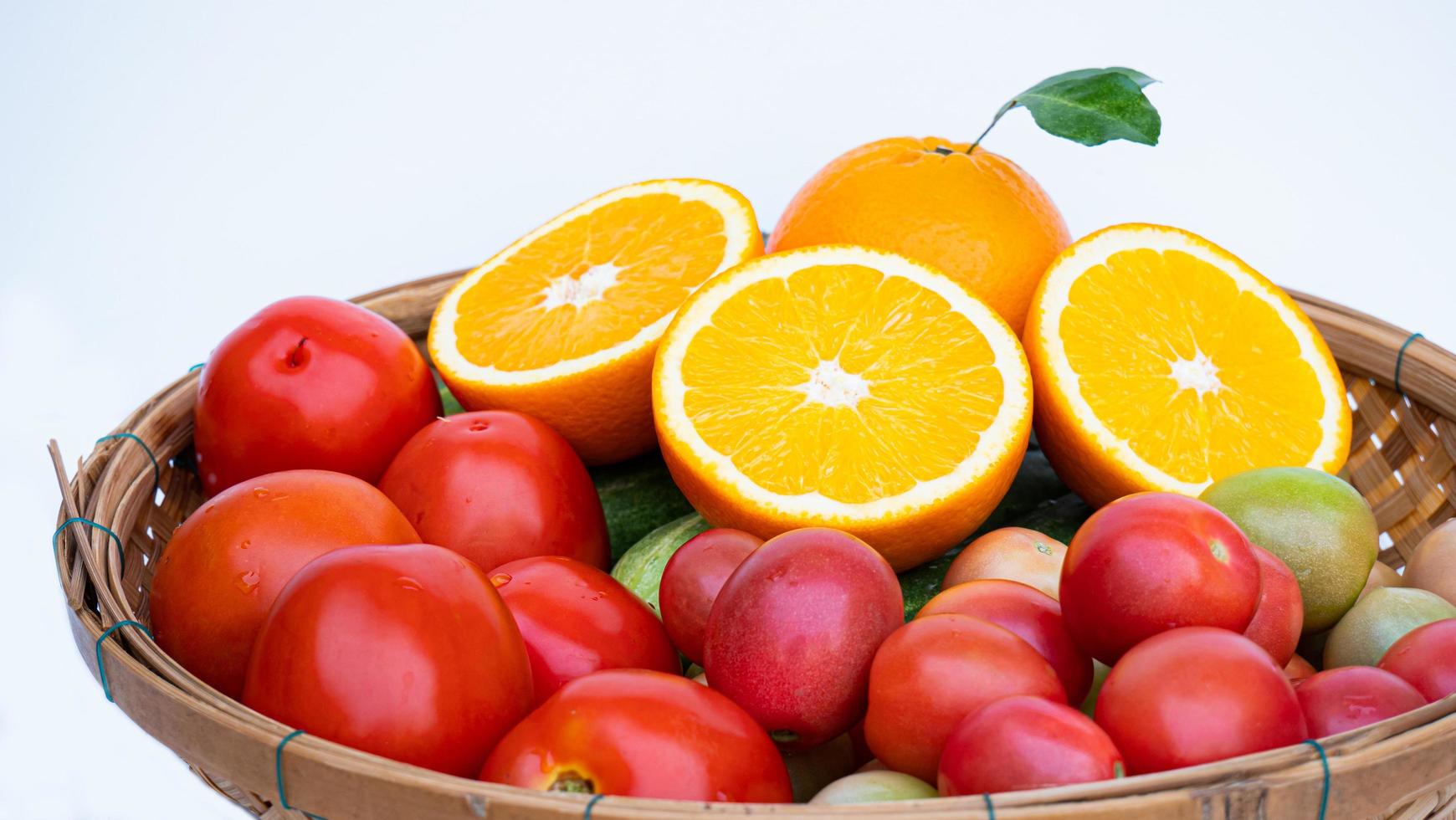half rijpe sinaasappel plaats een bamboemand met groenten en fruit met veel vitamine C, zoals rijpe sinaasappels, komkommers en tomaten op een witte achtergrond. foto