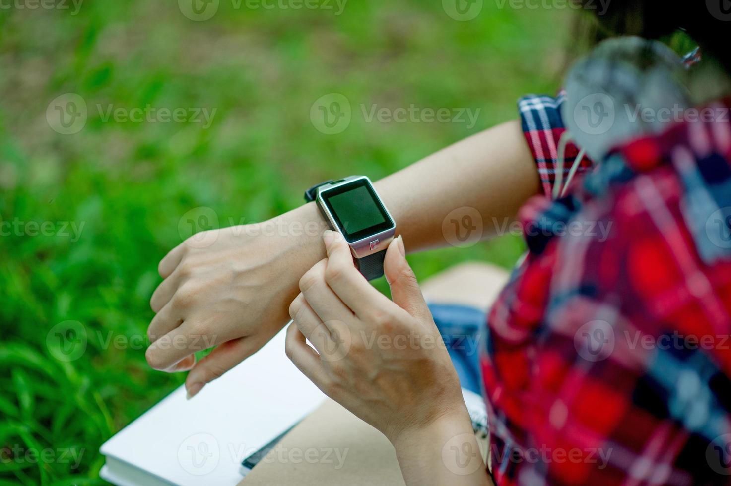 het meisje kijkt naar het horloge in de hand, kijkt naar de tijd in een zwart horloge, draagt een rood shirt en een groene achtergrond. en er is een kopie ruimte. foto