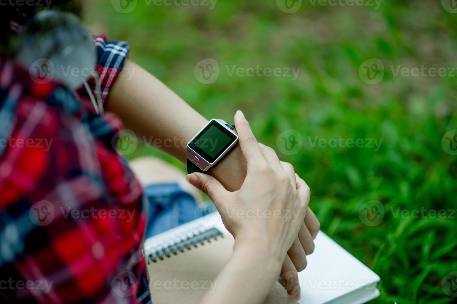 het meisje kijkt naar het horloge in de hand, kijkt naar de tijd in een zwart horloge, draagt een rood shirt en een groene achtergrond. en er is een kopie ruimte. foto