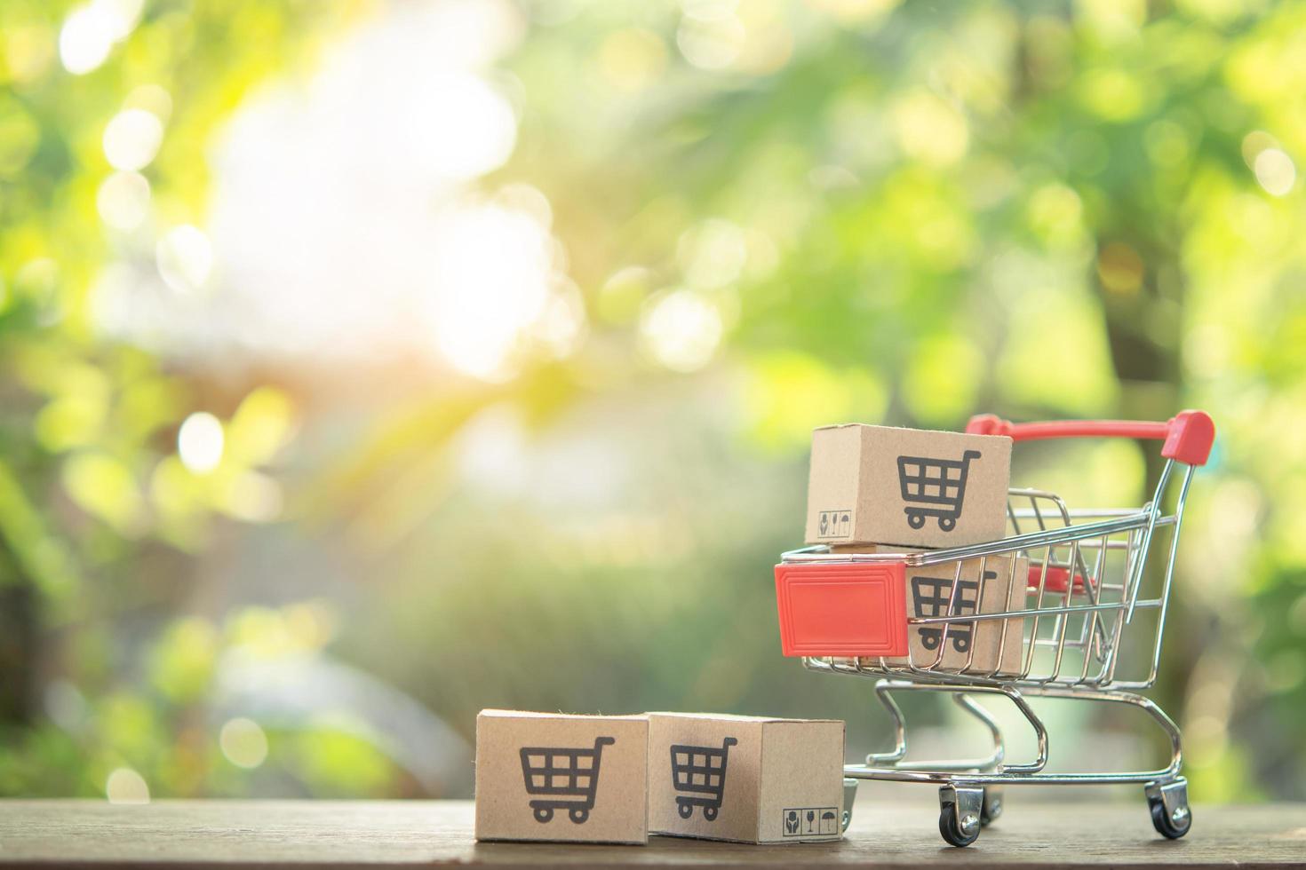 winkelconcept - winkelwagen of trolley en papieren dozen of pakket met een winkelwagen-logo op houten tafel. online winkelen consumenten kunnen winkelen vanuit huis en bezorgservice. met kopie ruimte foto