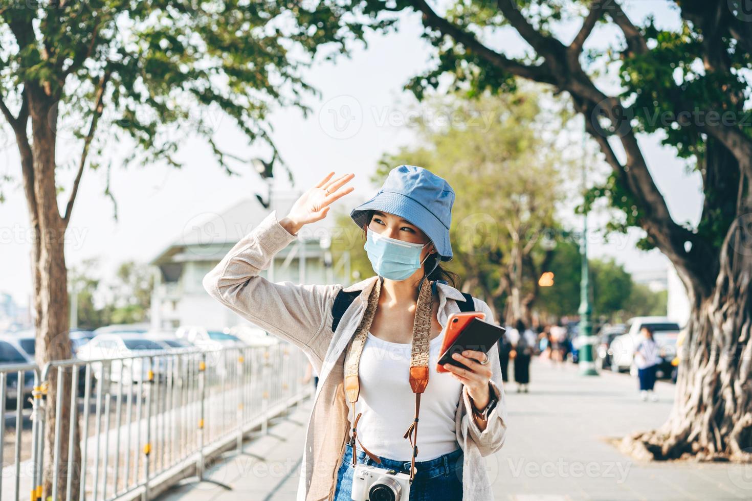 wandelende jonge volwassen aziatische vrouwelijke reiziger draagt een gezichtsmasker voor covid-19 die op zomerdag in de lokale stad reist. foto