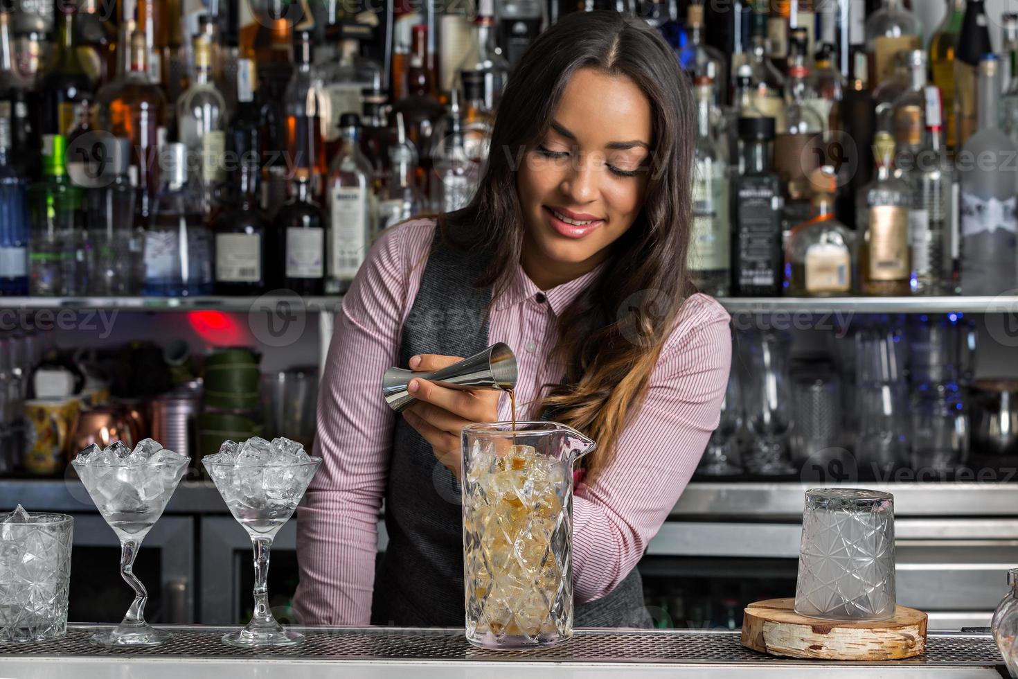 positieve vrouwelijke barkeeper die cocktail maakt in bar foto