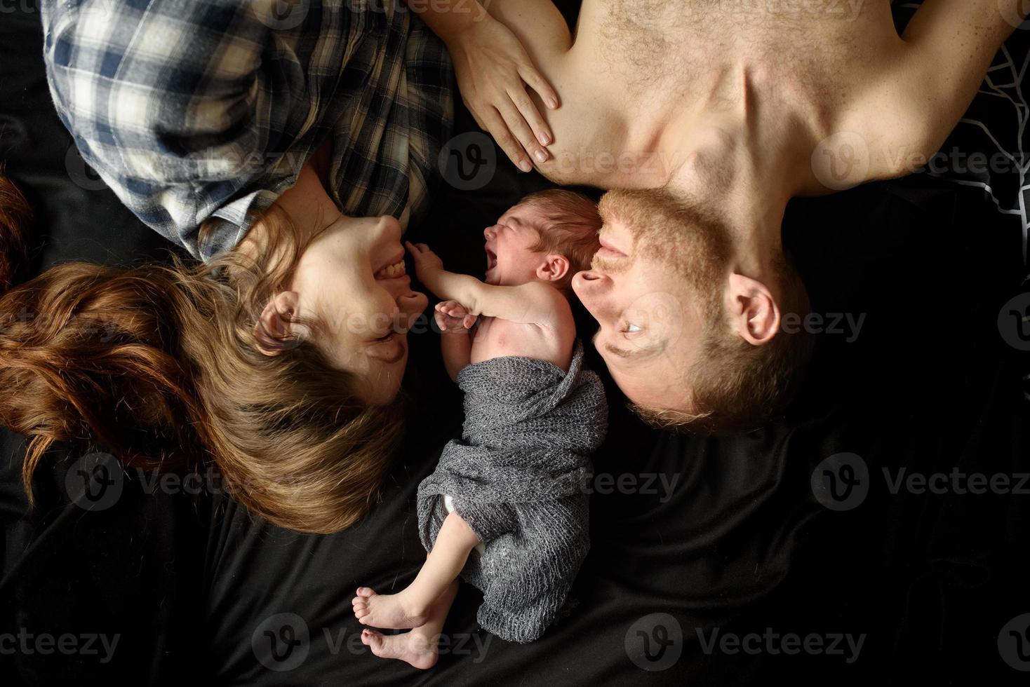 mama en papa staan naast hun pasgeboren zoon op een zwarte achtergrond. foto