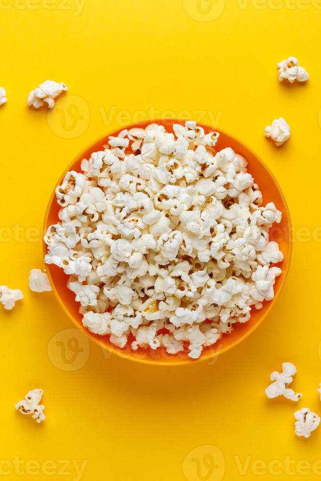 popcorn in een oranje kom op gele achtergrond. verticaal beeld. bovenaanzicht. foto