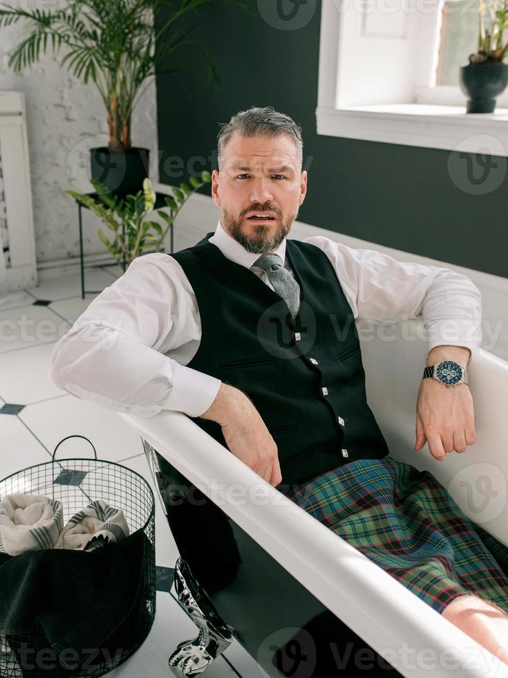 knappe volwassen moedige stijlvolle man scotsman in kilt en pak tot in de badkamer. stijl, thuiswerken, mode, lifestyle, lockdown, cultuur, etnisch concept. foto