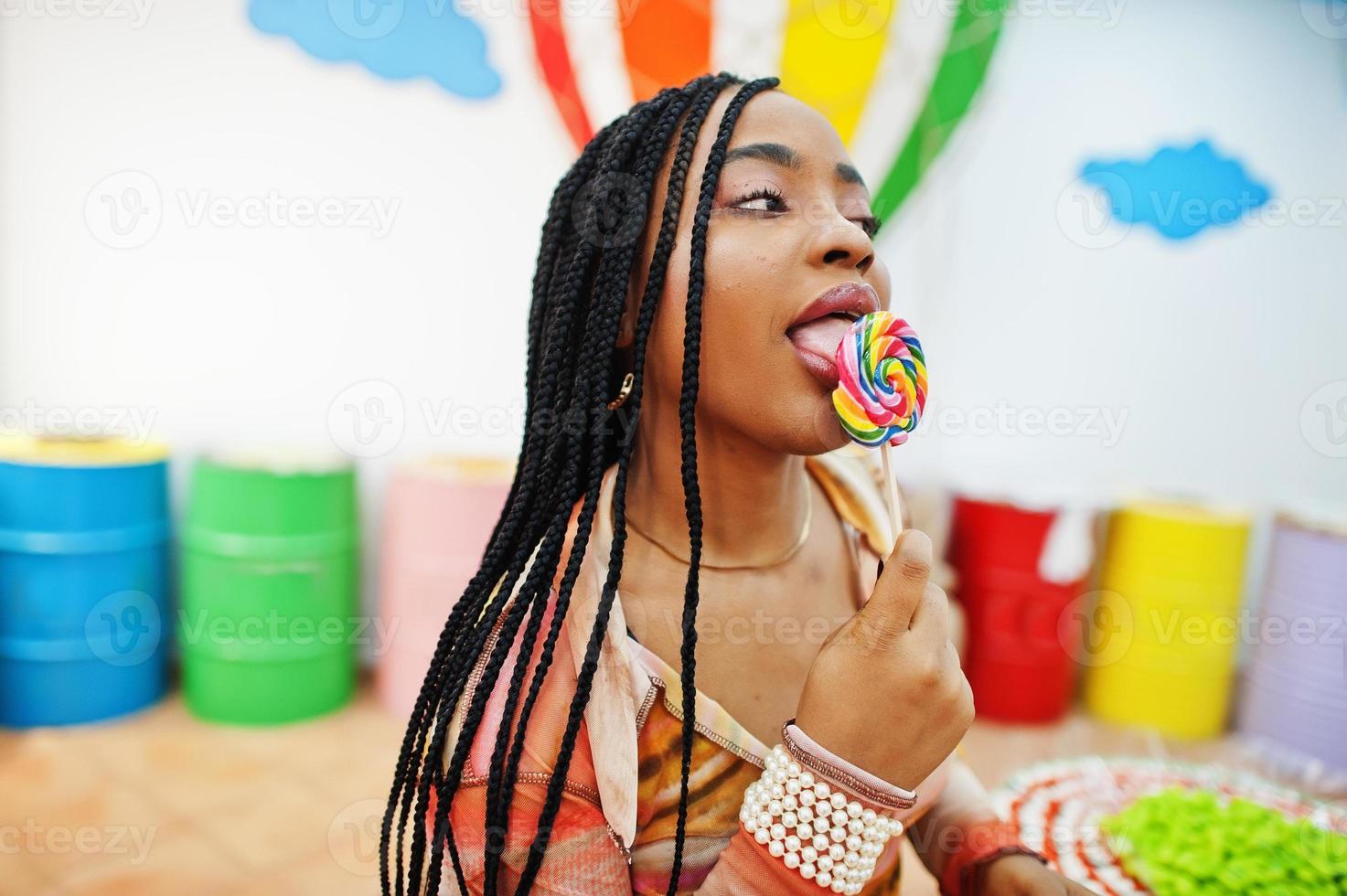 Afro-Amerikaanse duizendjarige dame bij snoepwinkel met lolipops. foto