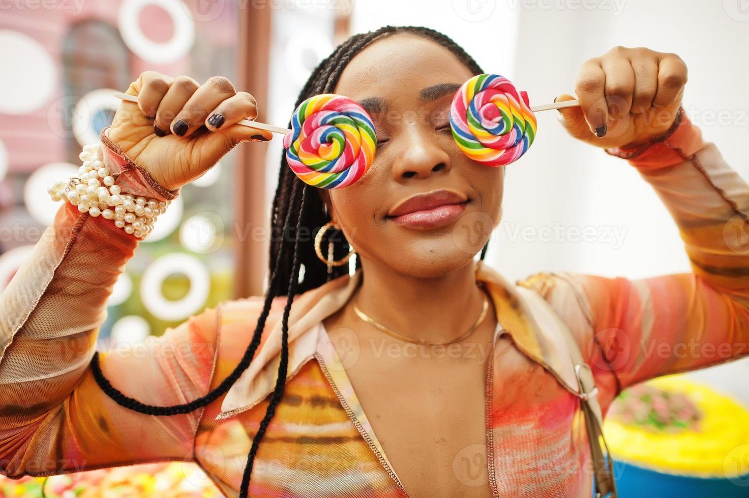 Afro-Amerikaanse duizendjarige dame bij snoepwinkel met lolipops bedekken haar ogen. foto