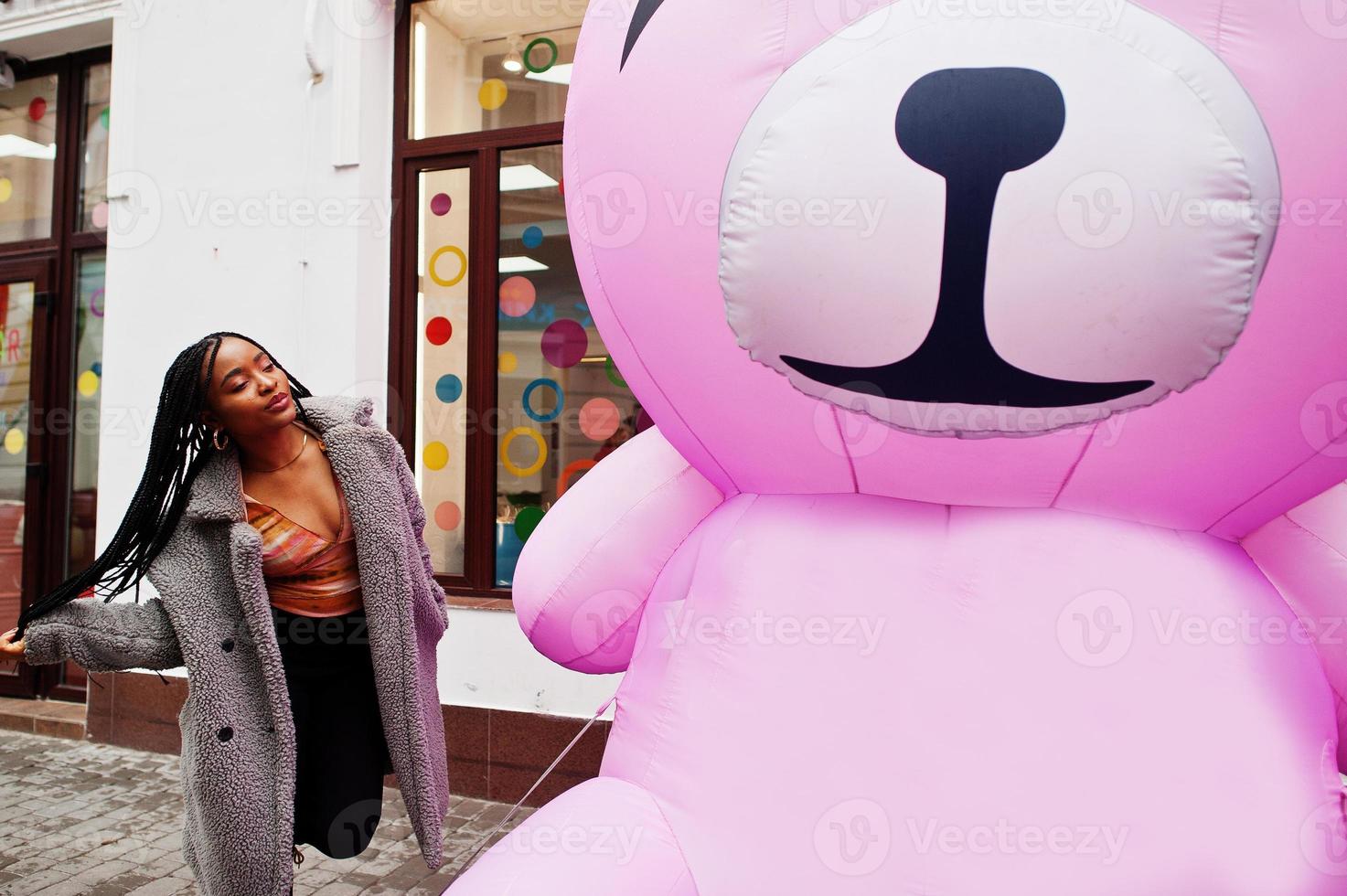 Afro-Amerikaanse duizendjarige dame in de buurt van opblaasbare roze teddybeer. foto